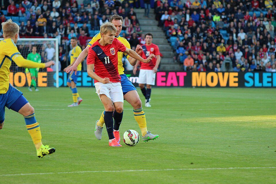 Ảnh tư liệu: Martin Odegaard (áo đỏ số 11 đội tuyển Na Uy) đi bóng qua hậu vệ Thụy Điển trong một trận đấu trên sân đầy khán giả. Nguồn: Wikimedia Commons.
