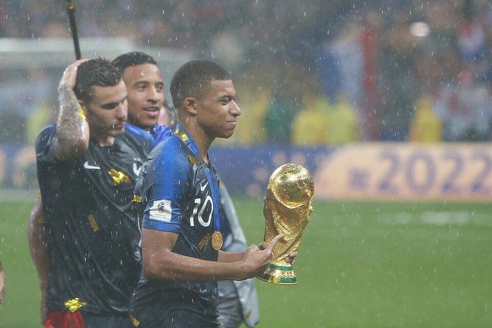Archive photo: Kylian Mbappé (France, No. 10) celebrating with teammates, holding the World Cup trophy in the rain. Source: Wikimedia Commons
